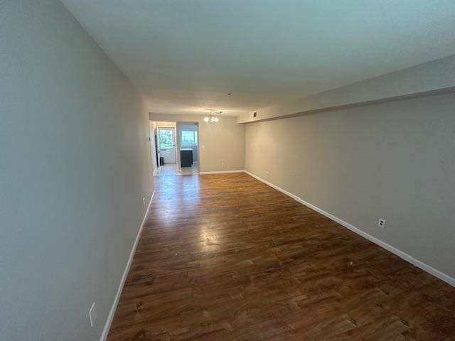 unfurnished room featuring an inviting chandelier, dark wood-type flooring, and baseboards
