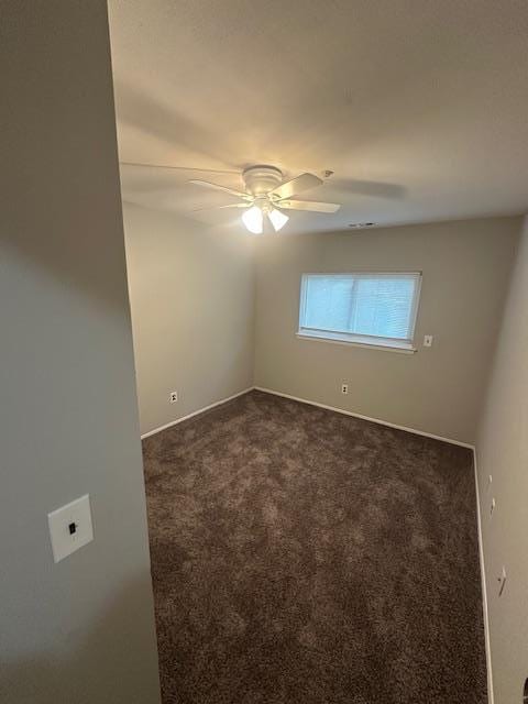 empty room with ceiling fan, dark colored carpet, and baseboards