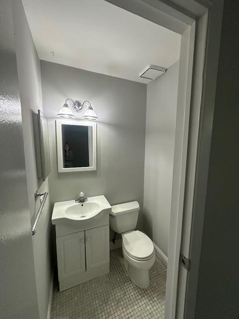 half bath featuring toilet, tile patterned flooring, vanity, and baseboards