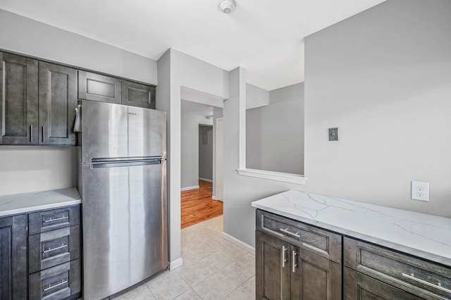 163 Pointe Cir N Unit 163, Coram, NY 11727 - kitchen with freestanding refrigerator, light tile patterned flooring, light stone countertops, baseboards, and dark brown cabinetry