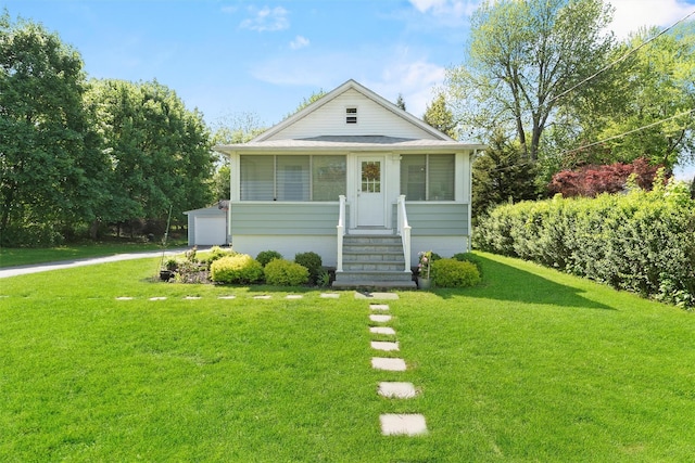 bungalow with a front lawn, entry steps, a detached garage, and an outbuilding