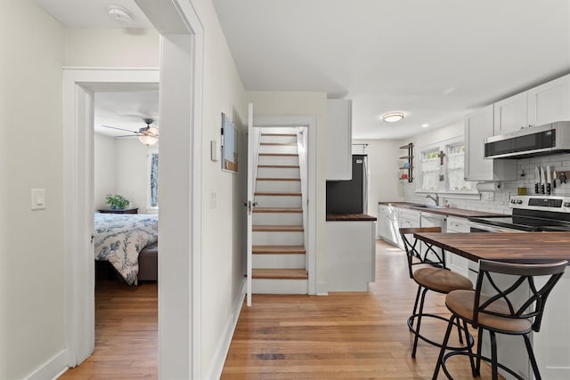 kitchen with stainless steel appliances, light wood-style flooring, backsplash, white cabinets, and wood counters