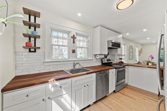kitchen with wood counters, stainless steel appliances, a sink, open shelves, and decorative backsplash