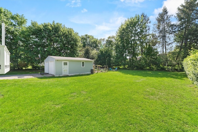 view of green lawn featuring a detached garage, an outdoor structure, driveway, and view of wooded area