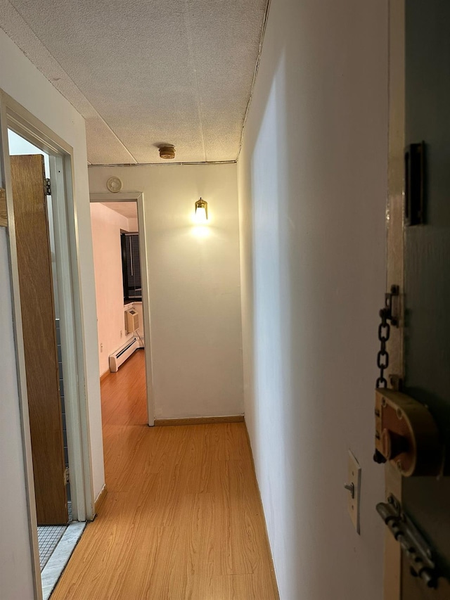 hall featuring baseboard heating, light wood-type flooring, and a textured ceiling