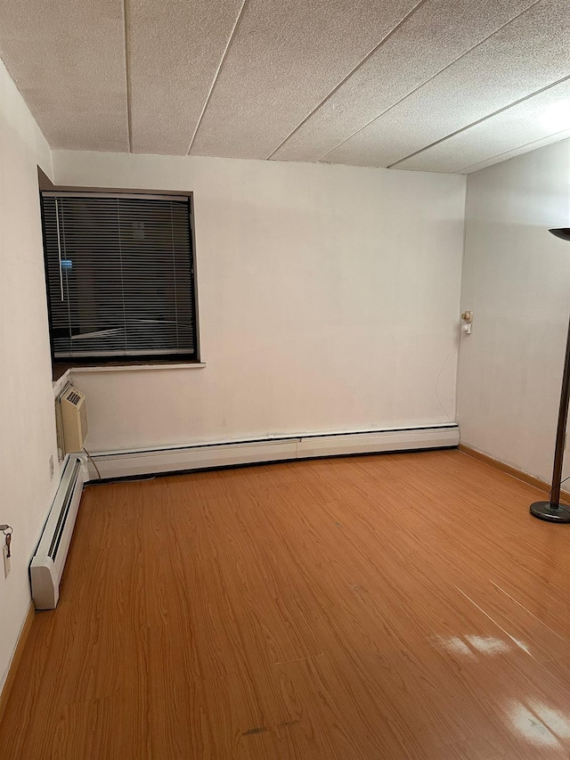 unfurnished room with a baseboard radiator, a wall unit AC, and wood finished floors