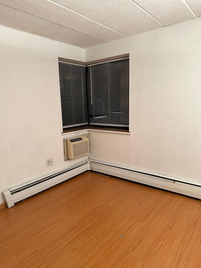unfurnished room with a baseboard radiator, a wall mounted air conditioner, and wood finished floors