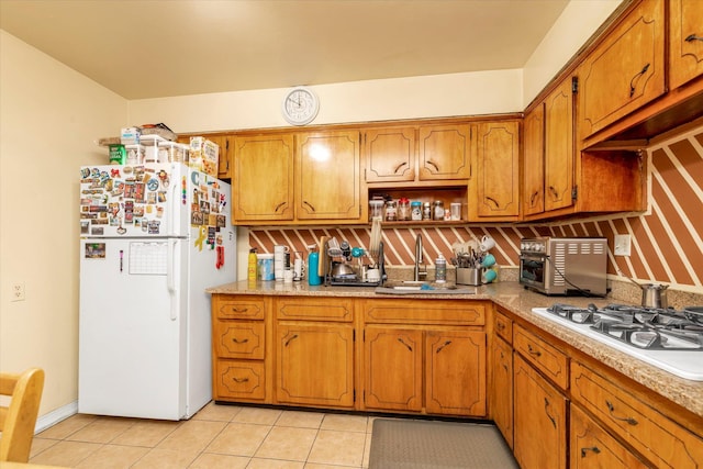kitchen with a sink, brown cabinetry, white appliances, and light tile patterned floors
