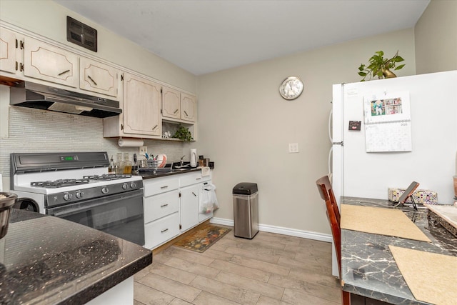 kitchen featuring under cabinet range hood, baseboards, light wood finished floors, gas stove, and backsplash