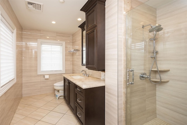 full bath with tile patterned floors, a shower stall, toilet, vanity, and tile walls