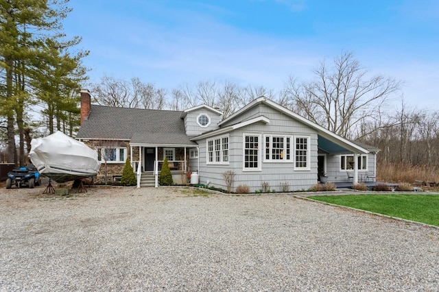 view of front of house with covered porch, a shingled roof, a chimney, and driveway