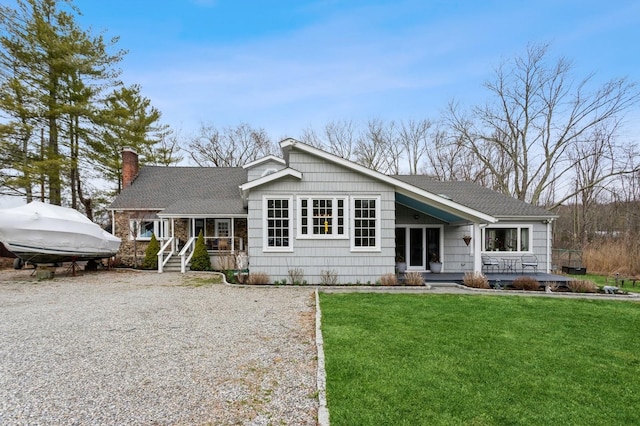 ranch-style home with a porch, a shingled roof, a chimney, and a front yard