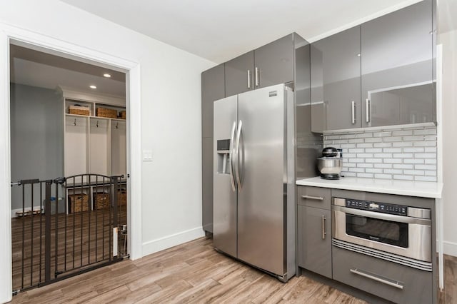 kitchen featuring tasteful backsplash, light wood finished floors, gray cabinetry, baseboards, and appliances with stainless steel finishes
