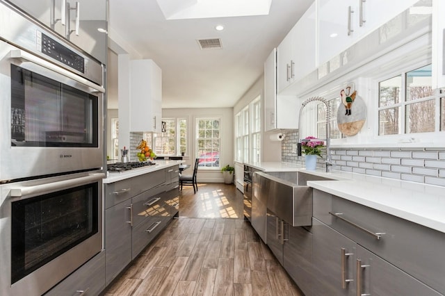 kitchen featuring gray cabinetry, appliances with stainless steel finishes, light countertops, and backsplash