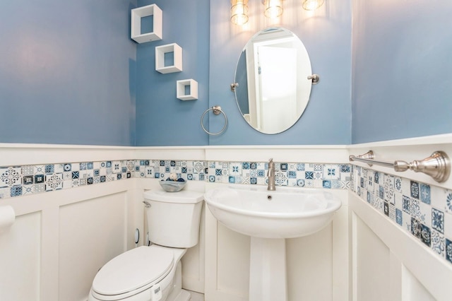 half bath with toilet and a wainscoted wall