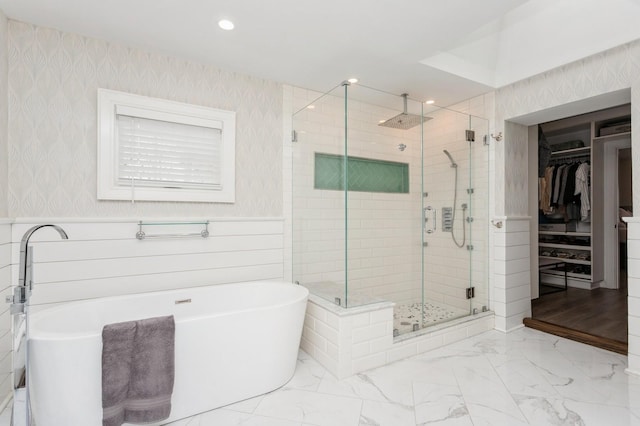 full bath with wallpapered walls, wainscoting, a shower stall, a freestanding tub, and a spacious closet
