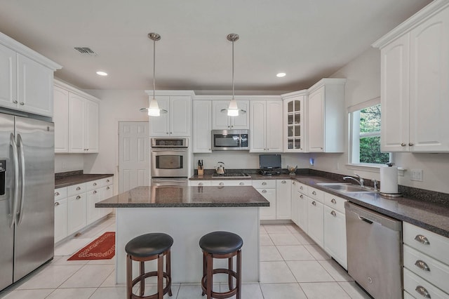 kitchen featuring stainless steel appliances, a sink, a kitchen island, white cabinetry, and light tile patterned floors
