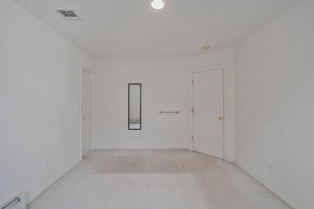 spare room featuring a baseboard heating unit, light colored carpet, and baseboards