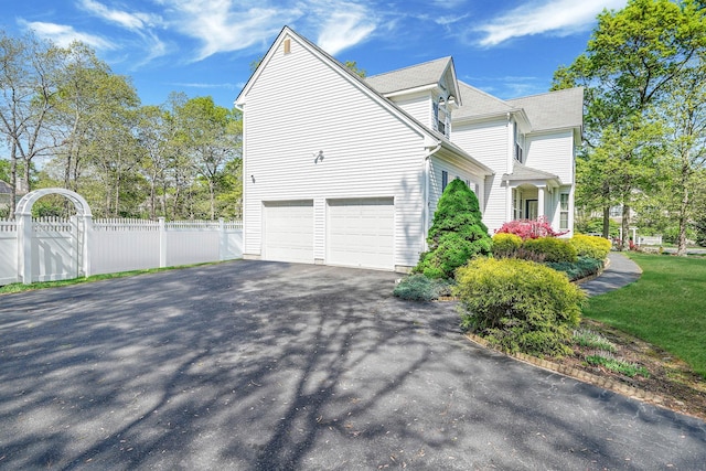 view of side of property with asphalt driveway, fence, and an attached garage