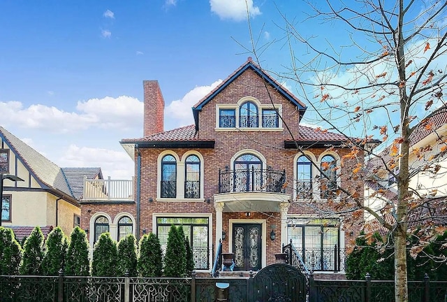 view of front of property featuring a fenced front yard, brick siding, a chimney, and a balcony