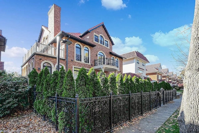 view of side of home with fence, a chimney, brick siding, and a balcony