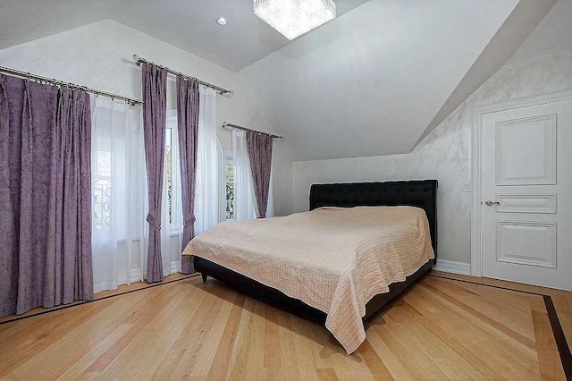 bedroom featuring baseboards, light wood finished floors, and vaulted ceiling