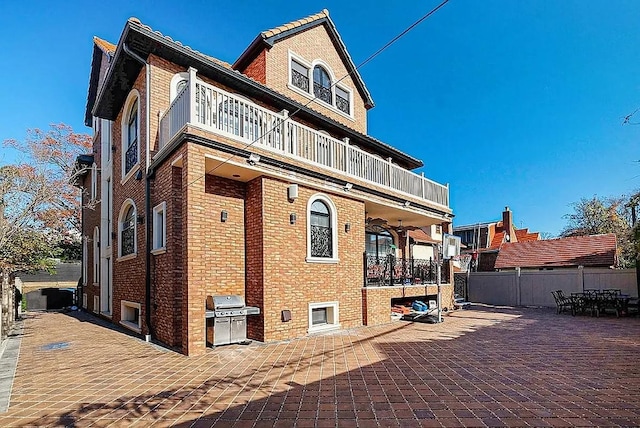rear view of house featuring a balcony, brick siding, and fence