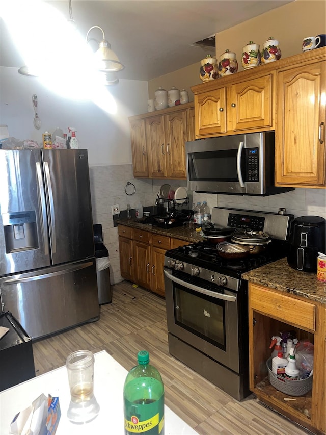 kitchen featuring appliances with stainless steel finishes, light wood finished floors, brown cabinetry, and tile walls