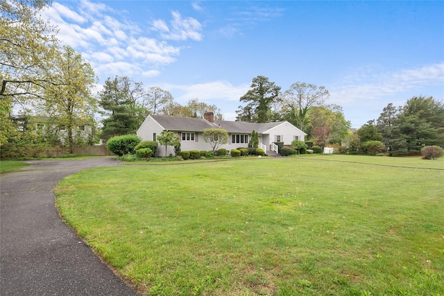 ranch-style home with a front lawn, a chimney, and driveway