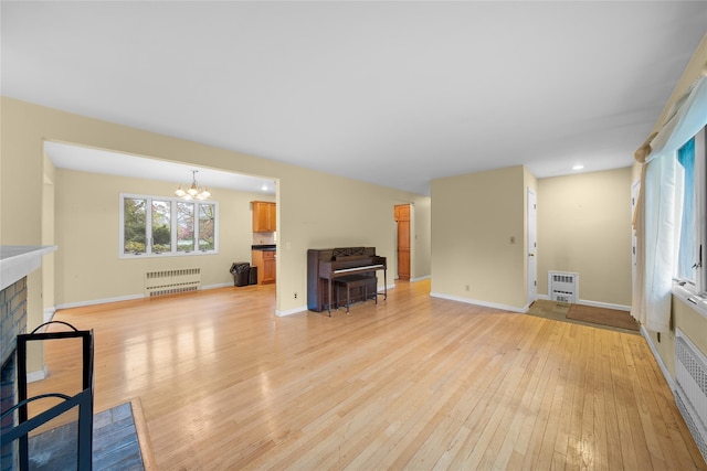 unfurnished living room featuring baseboards, radiator, an inviting chandelier, light wood-style floors, and a fireplace