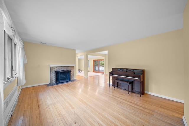 living room featuring baseboards, light wood-style floors, visible vents, and a brick fireplace