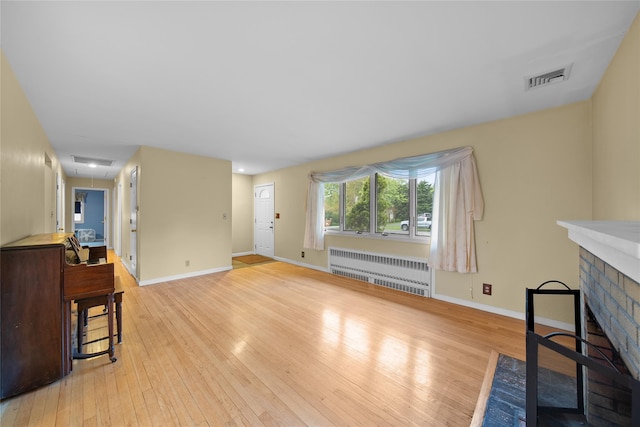 unfurnished living room featuring radiator heating unit, attic access, light wood-type flooring, visible vents, and baseboards