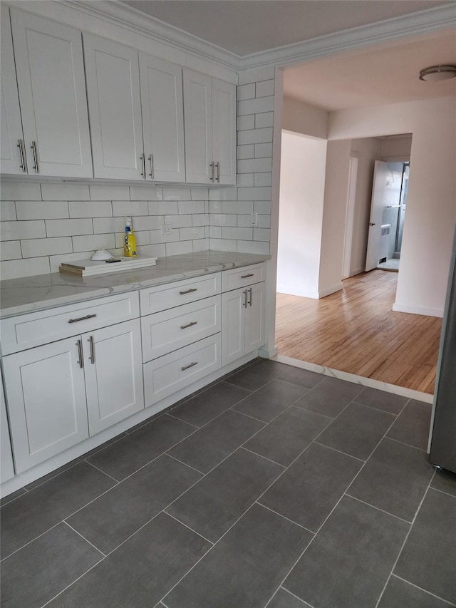 kitchen featuring light stone countertops, ornamental molding, dark tile patterned floors, white cabinetry, and decorative backsplash