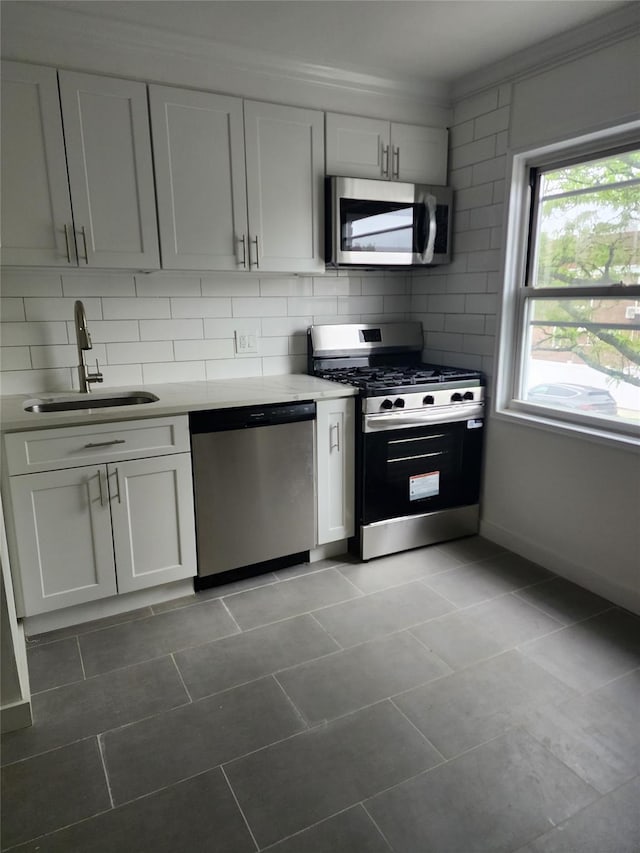 kitchen featuring a sink, ornamental molding, decorative backsplash, light countertops, and appliances with stainless steel finishes
