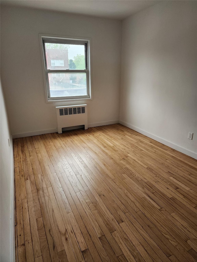 unfurnished room featuring hardwood / wood-style flooring, baseboards, and radiator heating unit