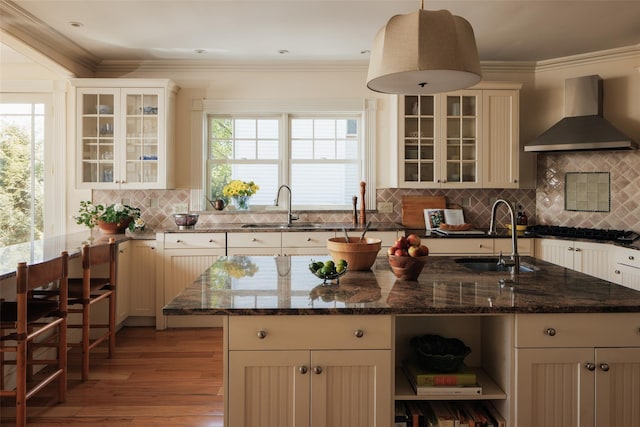 kitchen featuring open shelves, wall chimney exhaust hood, light wood finished floors, and a sink