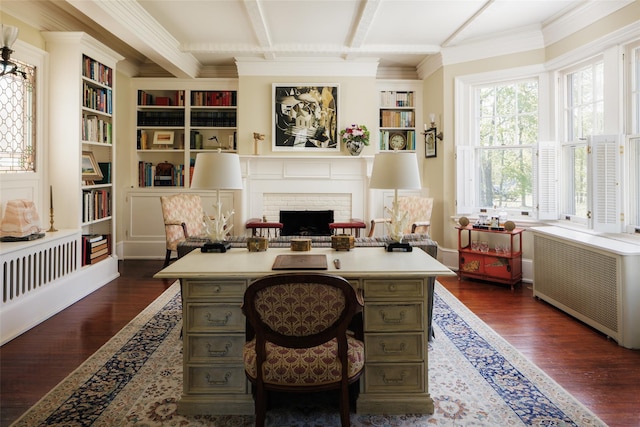 office area with radiator, beam ceiling, built in shelves, dark wood-style flooring, and a brick fireplace