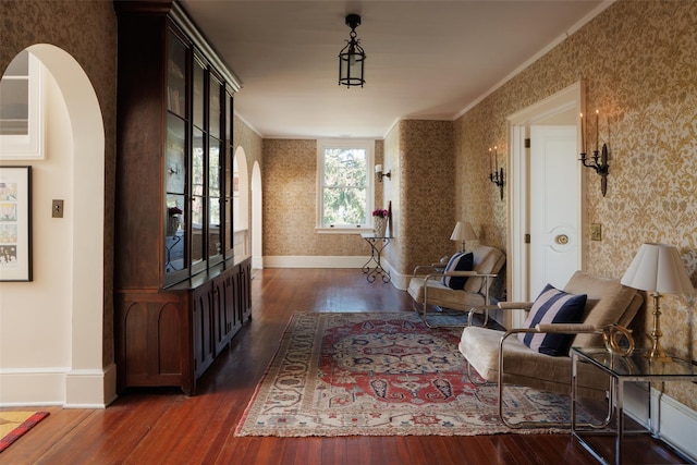 hall with crown molding, arched walkways, dark wood-style floors, and wallpapered walls