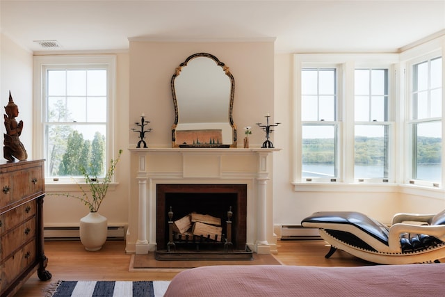 living area with a baseboard heating unit, a wealth of natural light, visible vents, and wood finished floors
