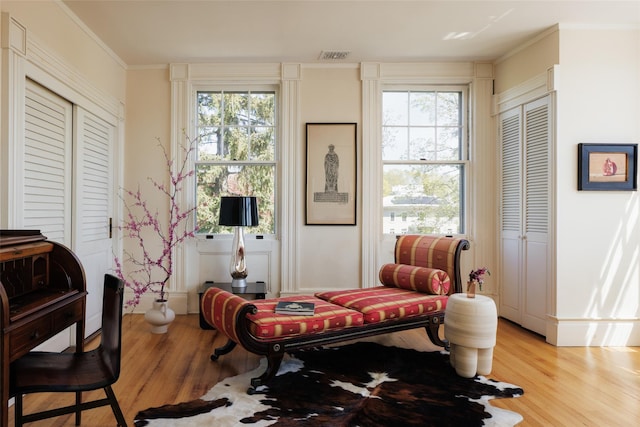 living area featuring light wood finished floors, crown molding, and visible vents