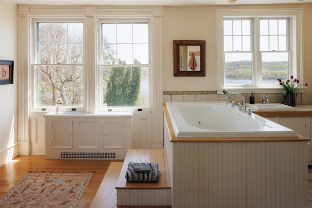 full bath with a sink, a whirlpool tub, visible vents, and wood finished floors