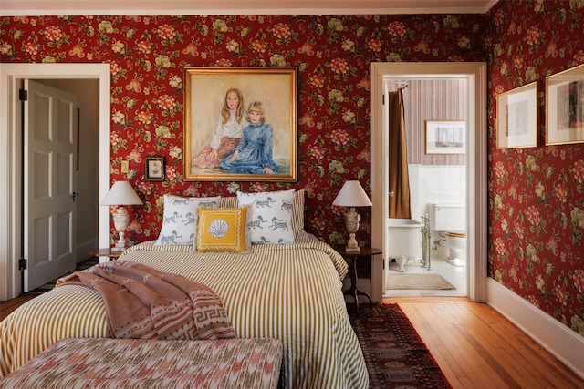 bedroom with wallpapered walls, ensuite bath, baseboards, and hardwood / wood-style flooring
