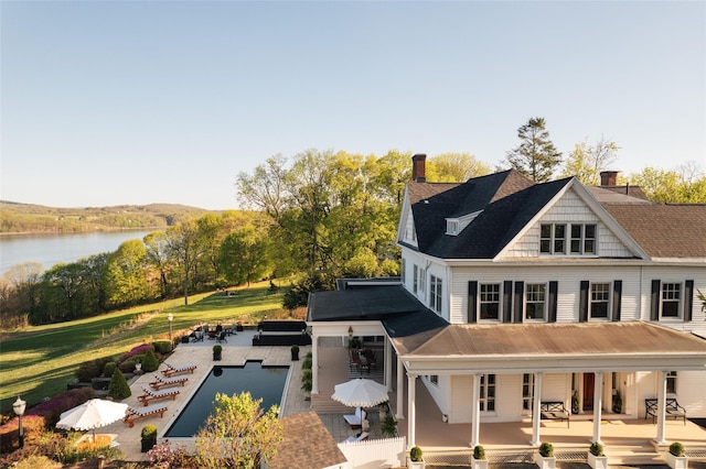 rear view of house with a porch, a water view, a chimney, and an outdoor pool