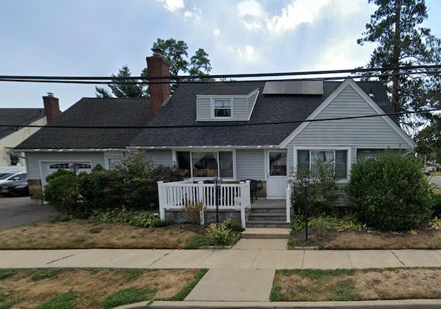 view of front facade featuring a chimney, a porch, solar panels, and a shingled roof