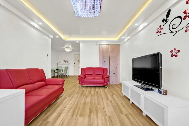 living area featuring a raised ceiling, light wood-style floors, a chandelier, and recessed lighting