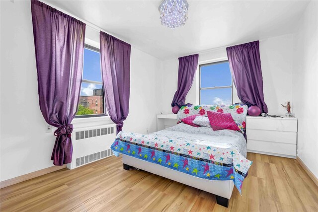 bedroom with radiator, multiple windows, wood finished floors, and baseboards