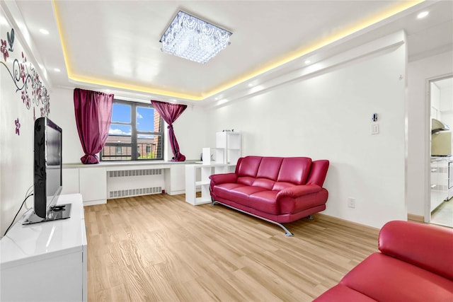 living area featuring radiator, light wood finished floors, recessed lighting, a raised ceiling, and baseboards