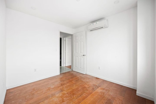 empty room with light wood-type flooring, baseboards, and an AC wall unit