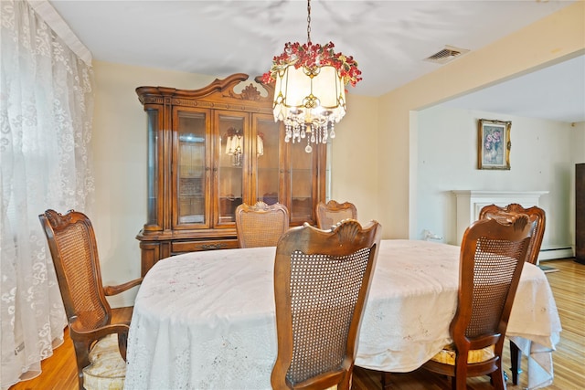 dining room featuring wood finished floors, a notable chandelier, visible vents, baseboards, and a baseboard heating unit