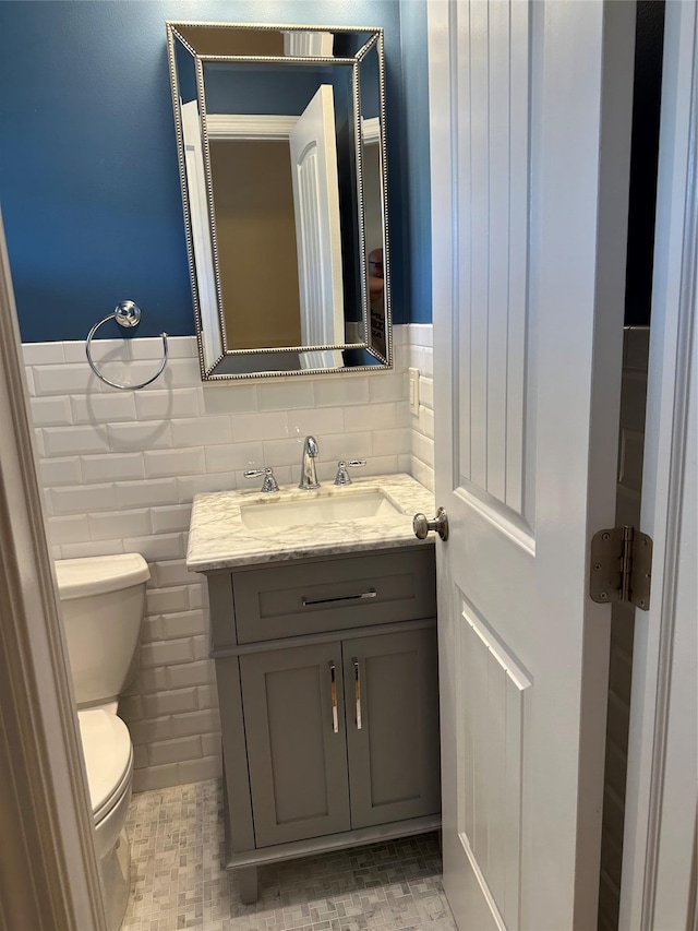 half bath with a wainscoted wall, toilet, tile walls, and vanity